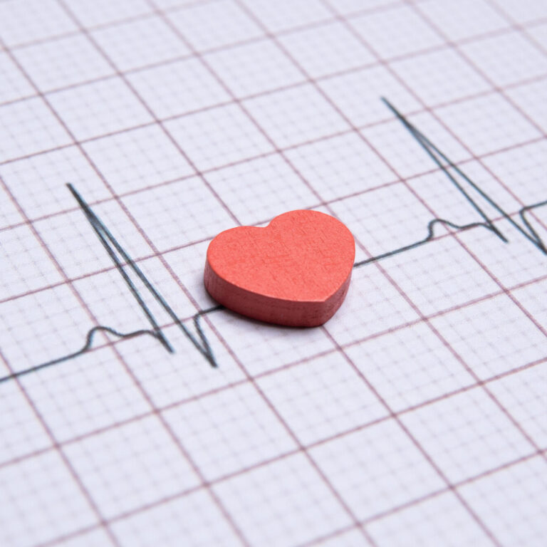 Closeup image of a red heart on a electrocardiogram (ECG) printout. The ECG graph shows a normal sinus rhythm. Healthy heart, wellbeing concept.