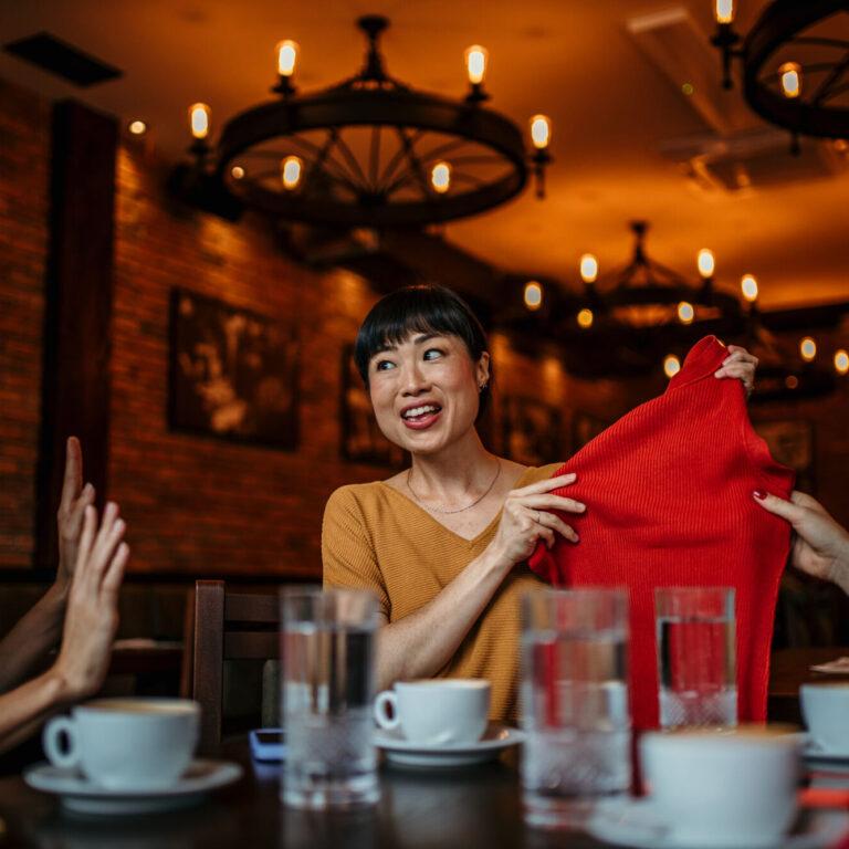 Happy women having a conversation at a table in a cafe, while one of them shows a red sweater