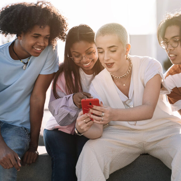 Group of friends sitting together using mobile phones to share content on social media