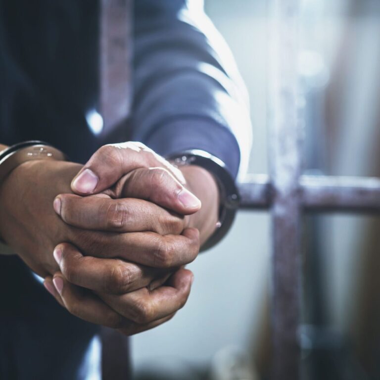handcuffed-hands-of-a-prisoner-behind-the-bars-of-2023-11-27-05-01-33-utc