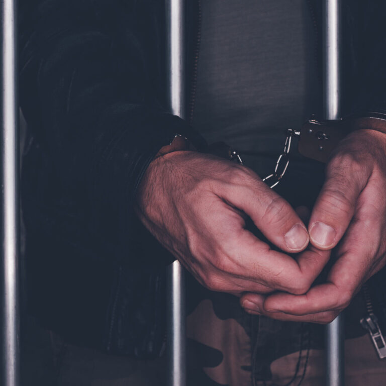 Handcuffed man behind prison bars. Arrested criminal male person imprisoned.
