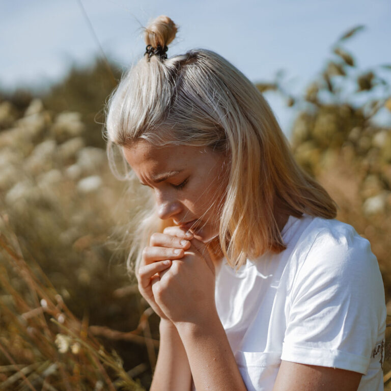 A teenage girl closed her eyes while praying in a field. Hands folded in prayer faith, spirituality and religion concept. Meditation