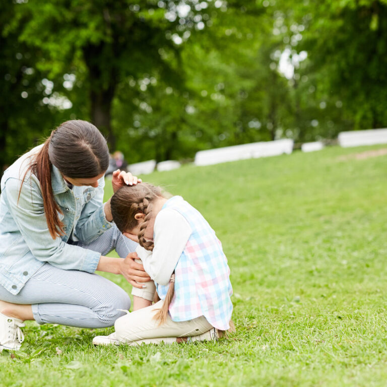 Little girl crying while sitting on green lawn and her mother comforting her