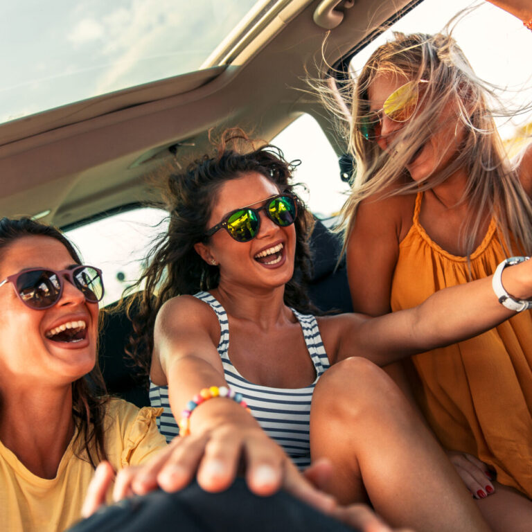Three female friends enjoying traveling in the car. Sitting in rear seat and having fun on a road trip.