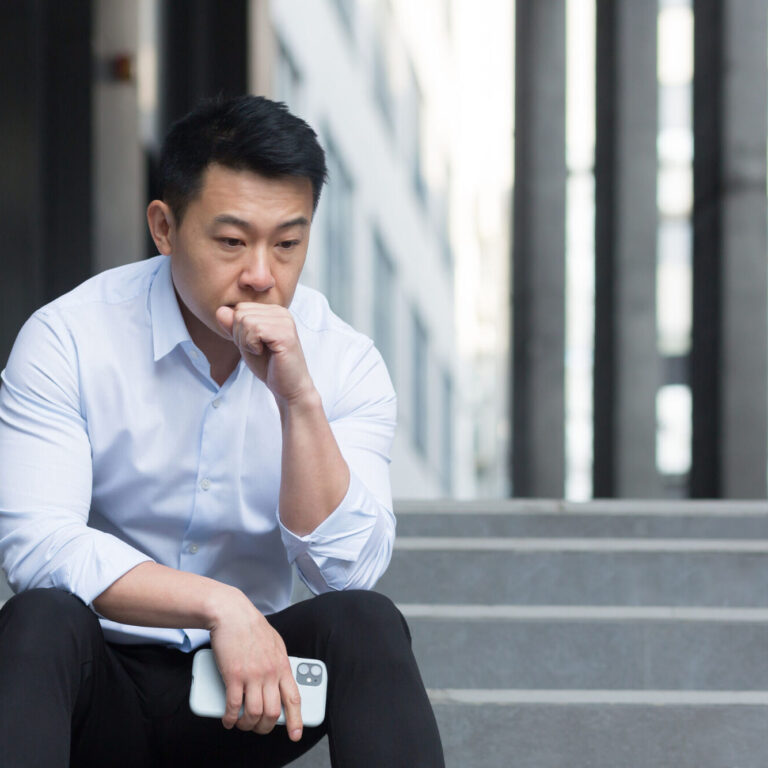 Upset Asian sitting on stairs outside office center, depressed man and frustrated businessman