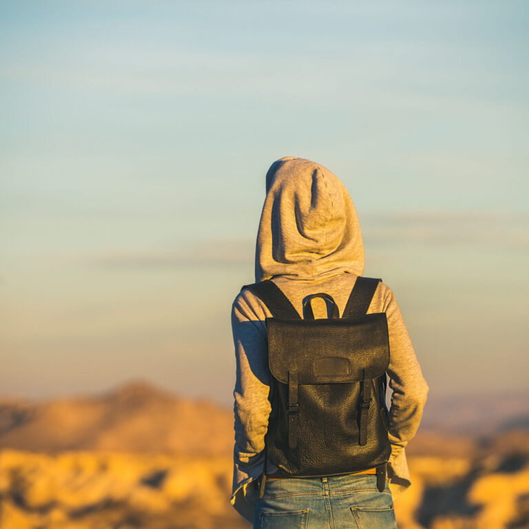 Young woman traveller wearing hoodie and backpack watching sunrise in the mountains over Goreme, Cappadocia, Central Turkey